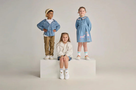 Three children standing on and around a white block wearing different colourways of Rafferty's Barefoot Sneakers.