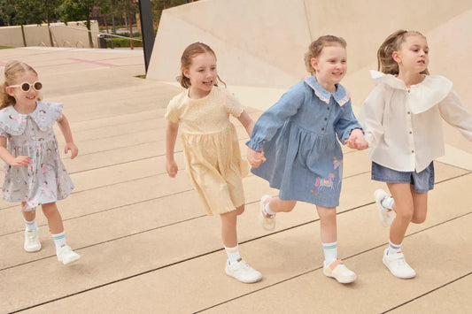 Four girls running outdoors wearing Rafferty’s Shoes barefoot sneakers, holding hands on a timber walkway.
